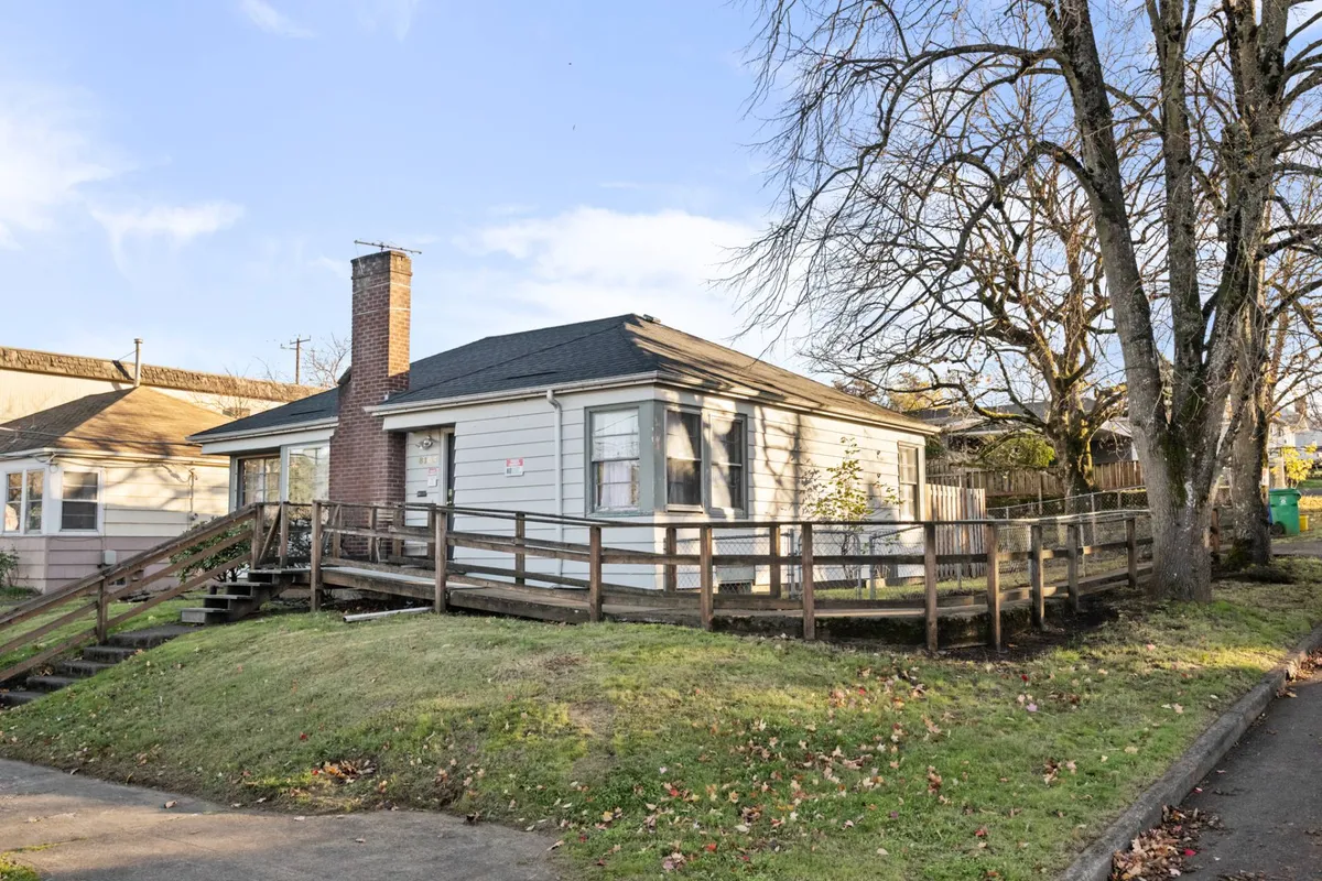 This image presents the exterior of the home, featuring the welcoming front porch, iconic chimney, and leafy trees surrounding the property. The scene conveys warmth and approachability, suggesting a quiet moment spent outdoors or friendly gatherings on the porch.
