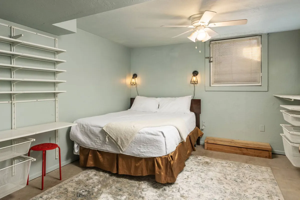 This image features a serene bedroom with a neatly made bed, inviting shelves, and soft lighting fixtures. The setting feels quiet and calm, suggesting a cozy atmosphere ideal for unwinding after a busy day.