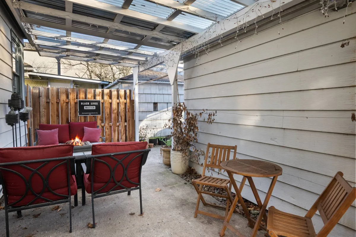 The cozy backyard fire pit area features red chairs arranged in a circle, a fire pit at the center, and a wooden fence with decorative signage in the background. The setup suggests intimate evenings spent outside, whether for relaxation or special celebrations.