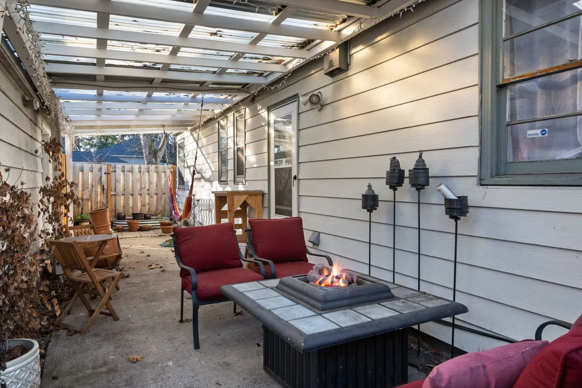 A cozy outdoor fire pit area with red chairs surrounding a wooden table, set in a private backyard. The scene evokes warmth and togetherness, ideal for group gatherings or quiet evenings. The inviting setup highlights opportunities for outdoor relaxation and fun.